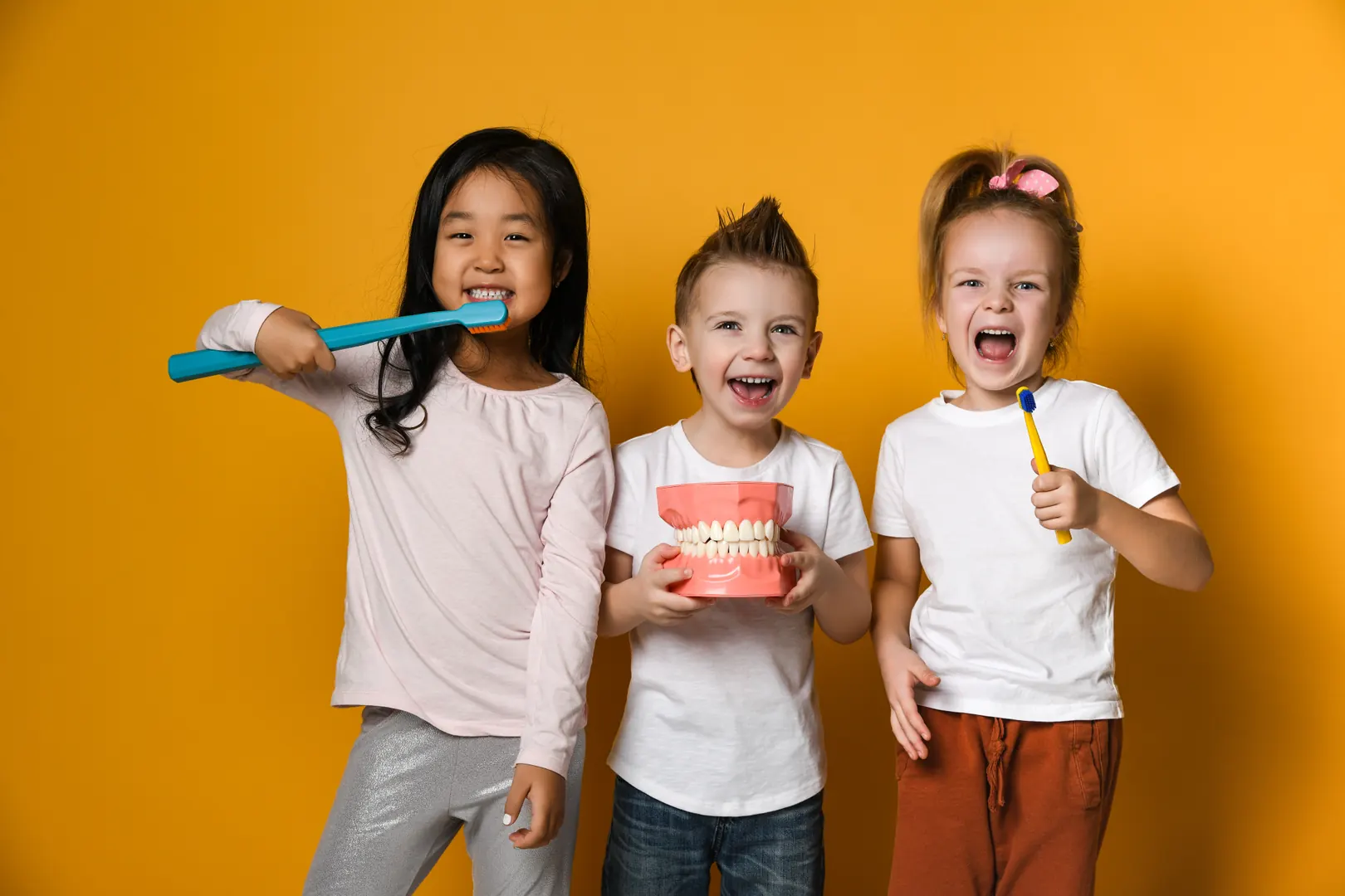 Three smiling children holding toothbrushes and a model of the teeth