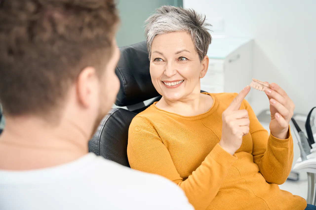 A patient holding her new dental bridge in the chair at Isom Dentistry
