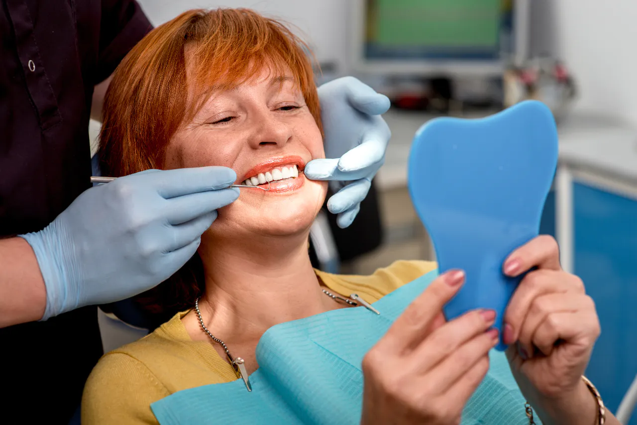 A patient seeing her completed dental implant in a hand mirror